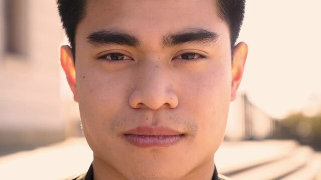 Outdoor portrait of an Asian man looking at the camera with a serious face and intense look. Close up of a serene human face - Concept of real people and emotions.