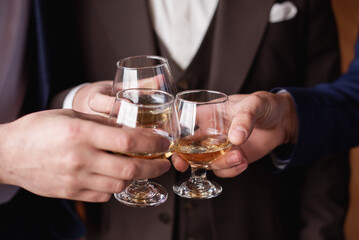 Groom with bestmen drinks whiskey from glasses. Closeup
