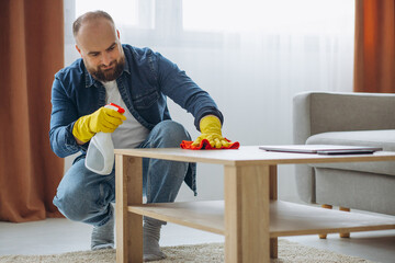 Man cleaning up at home wearing rubber gloves and using spray