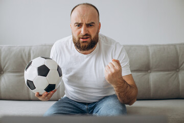 Man holding football ball and watching soccer online at home