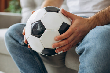 Man holding football ball and watching soccer online at home