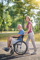 A woman carrying her husband in a wheel chair in a park