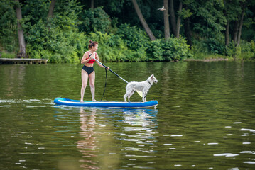 woman standing on paddle board with her white dog.