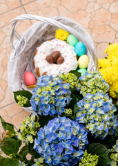 Congratulatory easter card. Easter cake with colored eggs in a white Easter basket. Basket decorated with blue and yellow flowers. Blue hydrangea and yellow chrysanthemum and Easter decor.