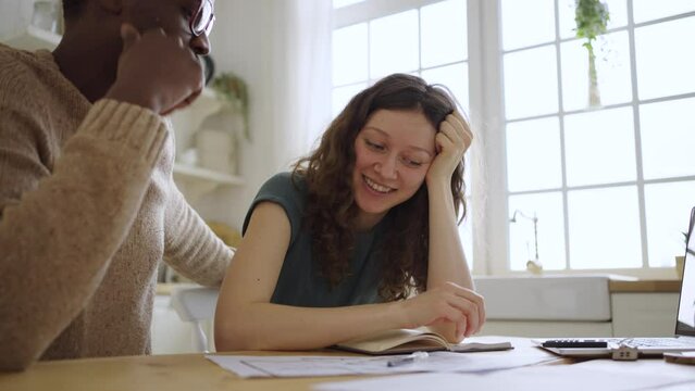 Realtor and female client sign contract of apartment purchase. African American man and white woman with curly hair talk and laugh in kitchen closeup