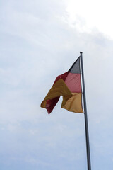 Close up of the national flag of Germany on Reichstag rooftop in summer waving high in the air. Black, red and gold horizontal stripes. Cloudy blue sky in background. No people.