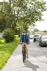 food shipping, health and people concept - delivery man in bike helmet and protective medical mask with thermal insulated bag and smatphone riding bicycle on city street