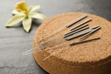 Cork coaster with acupuncture needles on black table, closeup
