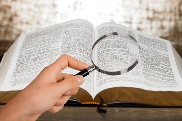 A magnifying glass in hand with open bible book. - obrazy, fototapety, plakaty