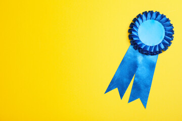 Blue award ribbon on yellow background, top view. Space for text