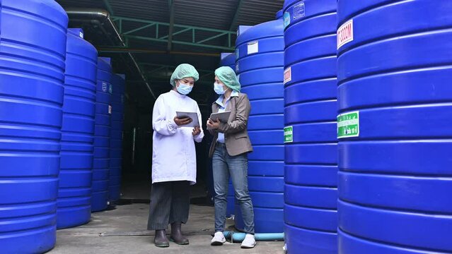 Asian Supervisor Woman Standing And Consulting With Employee Woman About Maintenance Of Water Tank System In Beverage Processing Plant