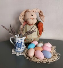 Easter bunny, easter eggs,porcelain vase with dry lavender branches.Gray background.Happy Easter.Rabbit with carrot.