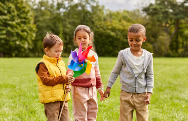 Fototapeta na wymiar childhood, leisure and people concept - happy kids with pinwheel having fun at park