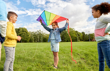 childhood, leisure and people concept - group of happy kids with kite playing at park