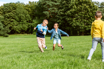 Obraz na płótnie Canvas childhood, leisure and people concept - group of happy kids playing tag game and running at park