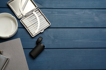 Open case with tobacco filter cigarettes, lighter and ashtray on blue wooden table, flat lay. Space for text