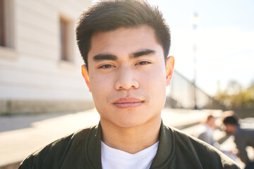 Outdoor portrait of an Asian man looking at the camera with a serious face and intense look. Close...