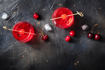Cocktail cherry and a mocktail on a dark background, a vibrant red drink with ice, two glasses, an overhead shot with a place for text