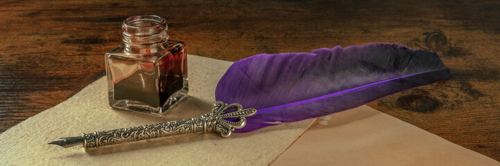 A quill pen with a vintage inkwell and some old paper on a dark rustic wooden desk, a panorama