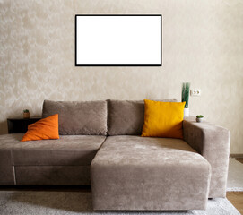 .white sheet of paper in a frame hangs on the wall above the new light gray sofa next to a beige wall. two orange pillows on the sofa and houseplants near the sofa. mockup