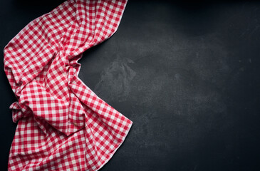 Folded red and white cotton kitchen napkin on a wooden black background, top view, copy space