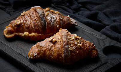 Baked croissants on a black wooden board sprinkled with powdered sugar, top view