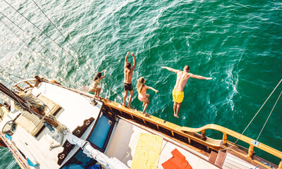 Top view of trendy adventurous friends jumping from sailboat on sea ocean trip - Millennial guys and girls having fun at exclusive boat party - Luxury vacation life style concept on bright filter - 500941377