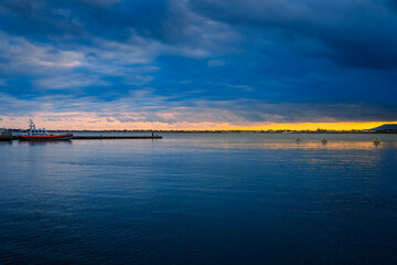 Sunset on the sea with cloudy sky and small harbor with dinghy and people