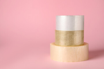 Three rolls of adhesive tape on pink background. Space for text