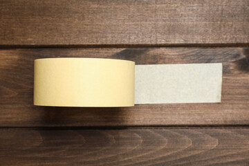 Roll of yellow adhesive tape on wooden background, top view