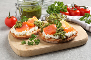 Delicious bruschettas with salmon, cream cheese and pesto sauce on light grey table