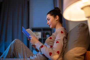 people, bedtime and rest concept - teenage girl reading book in bed at home at night - obrazy, fototapety, plakaty