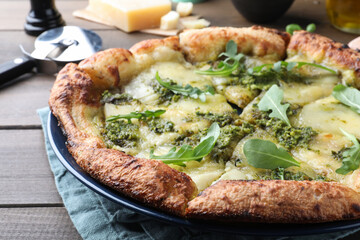 Delicious pizza with pesto, cheese and arugula on wooden table, closeup