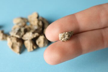 Woman holding kidney stone above light blue background, closeup. Space for text