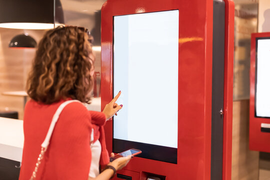 A girl orders food and lunch at a fast food restaurant using a self-service kiosk or a terminal with a screen. Modern commerce equipment