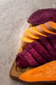 Whole And Cut Raw Orange And Purple Sweet Potato On Cutting Board Closeup, Top View