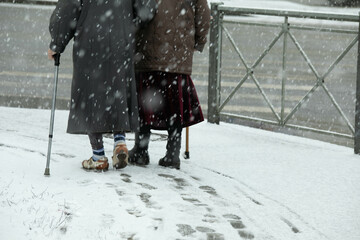 Two elderly women walk along the snow-covered alley. Healthy lifestyle of pensioners.