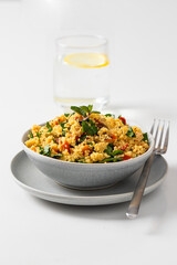 Healthy vegetarian salad with  chopped parsley, tomatoes, mint, onion, bulgur and seasoned with olive oil and lemon juice on the restaurant table with glass of water.