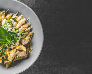 Penne pasta with chicken meat, cream sauce and cheese in a bowl on Dark grey black slate background