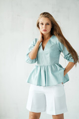 Nice girl in blue shirt and white shorts at grey wall. Summer women's wardrobe.