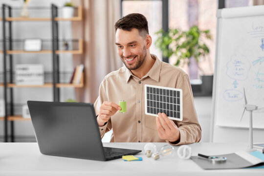 distance education, school and green energy concept - happy smiling male teacher with laptop computer and solar battery model having online class at home office