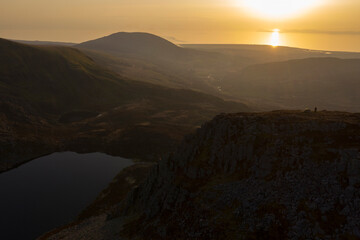 High aerial view of a man and a wild camping tent at the top of a mountain at sunset in Wales UK