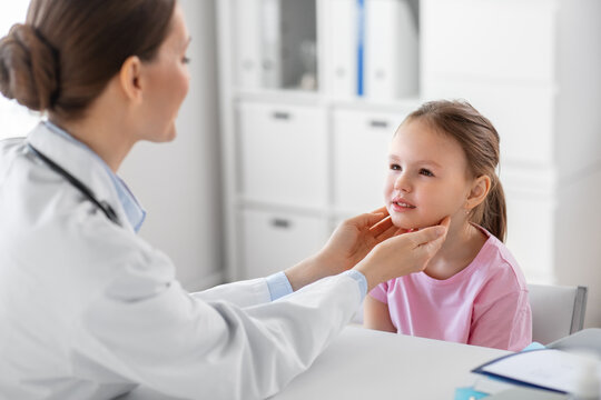 medicine, healthcare and pediatry concept - female doctor or pediatrician checking little girl patient's tonsils on medical exam at clinic