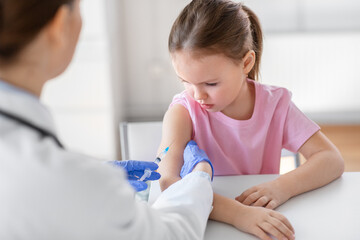 Obraz na płótnie Canvas medicine, healthcare and vaccination concept - female doctor or pediatrician with syringe making vaccine injection to little girl patient at clinic
