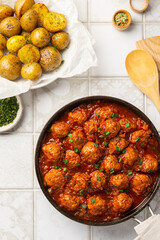 Meatballs in tomato-vegetable sauce with green onions, baked baby potatoes with dill on a tile background. Lunch time concept. View from above