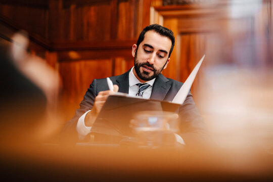 Confident bearded businessman with contract file sitting in board room during meeting