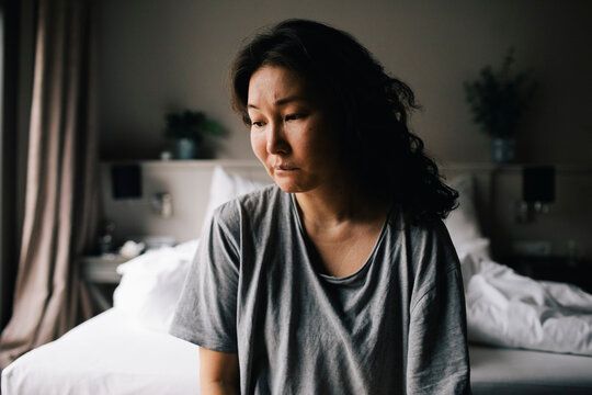 Lonely depressed woman looking down sitting in bedroom at home