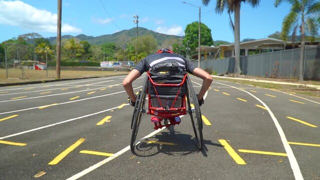 A kid with disability driving a handbike at a paracycling race. Handheld slow motion tracking shot (back of the bike running on the track).