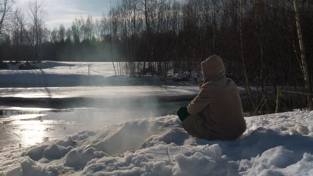 Portrait of man by frozen river stream, surviving in wild winter nature