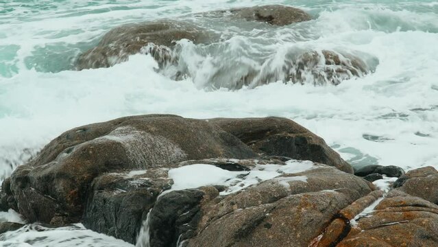 Close-up of sea waves breaking on rocks. White sea foam bubbles on the surface of the water. Dramatic sea on a gray cloudy day. Marine patterns. Beautiful waves in a storm.